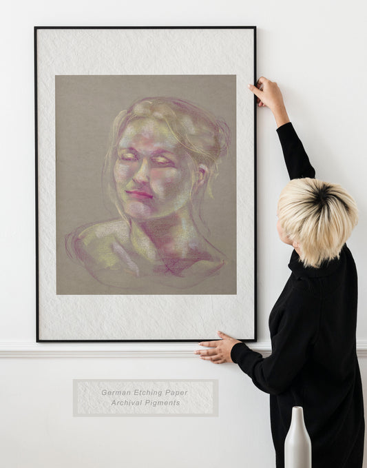 Woman holding framed Soft Glow fine art print by Bogdan Jensen on a wall, showing a soft pastel portrait in pale pink, yellow, and violet tones