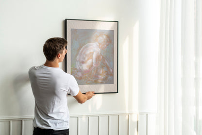 Person hanging framed Inner Stillness fine art print by Bogdan Jensen on a wall, showing the scale of the crouched figure study