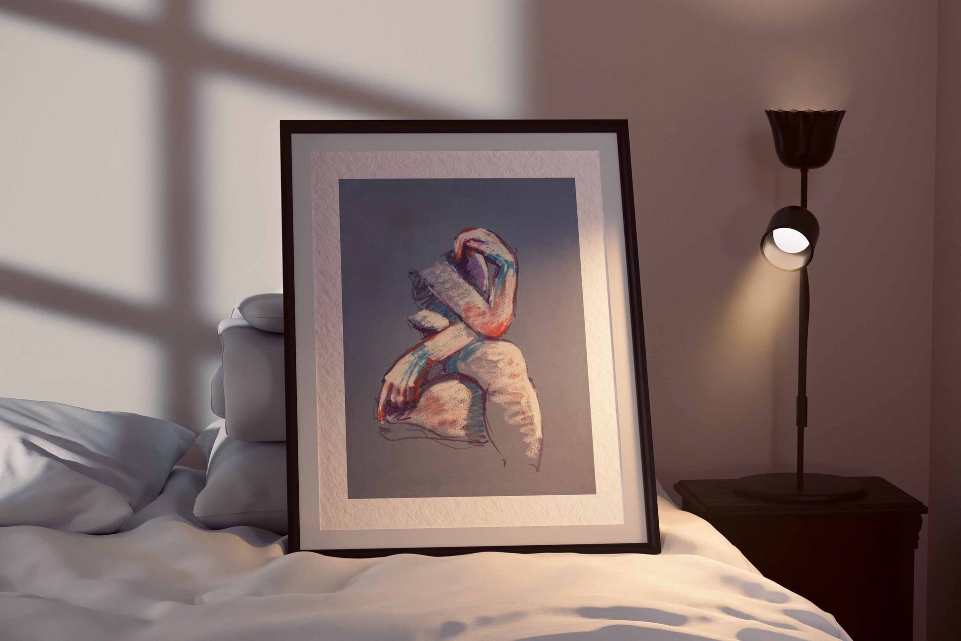 A Gentle Touch fine art print by Bogdan Jensen shown framed beside a bed, with the seated figure softly lit in pale pink, white, and blue pastel tones