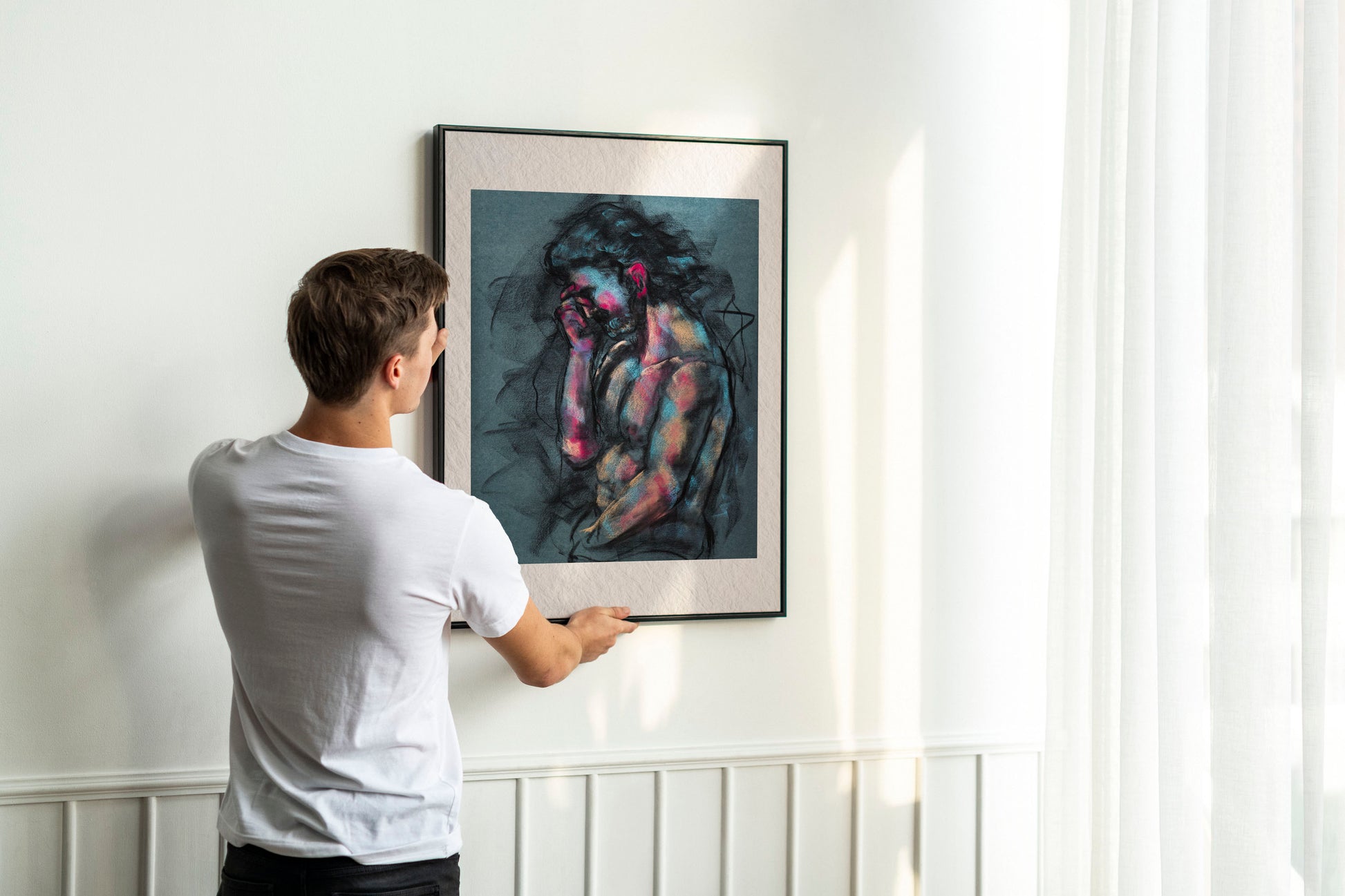 Person holding up framed A Quiet Ache fine art print by Bogdan Jensen on a wall, showing the charcoal figure drawing with blue and rose highlights in a bright interior
