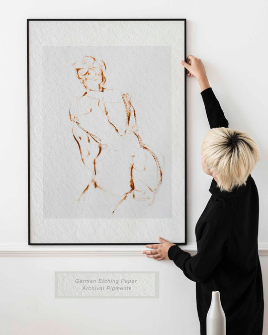 Lady holding framed A Shape I Almost Knew fine art print by Bogdan Jensen on a wall, showing the minimal brown line figure drawing in a bright interior