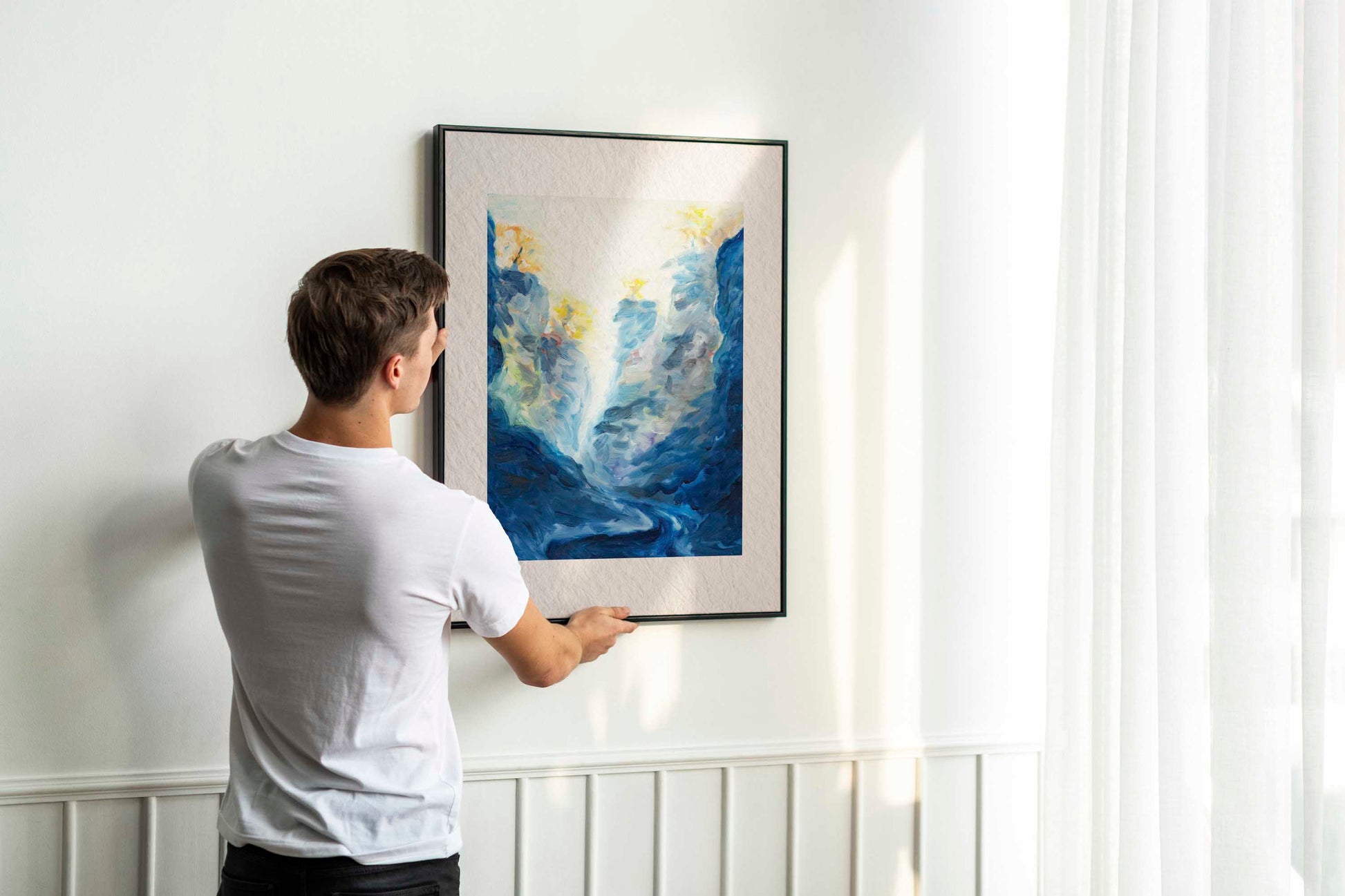 Person holding up framed Blue Passage fine art print by Bogdan Jensen on a wall, showing the blue-toned painting in a bright interior