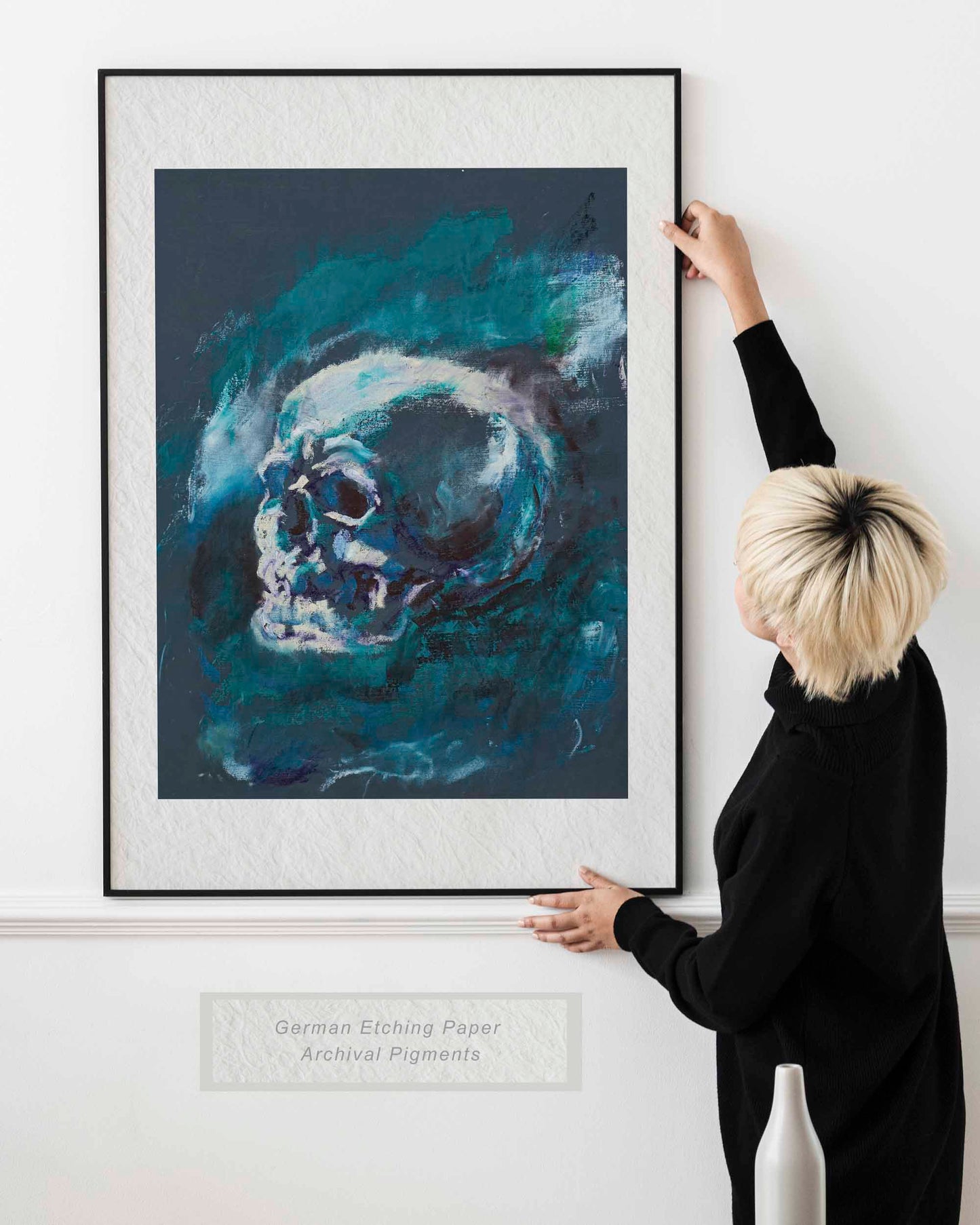 Woman holding framed Blue Remains fine art print by Bogdan Jensen on a wall, showing a blue-toned skull study in a bright interior