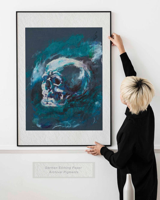 Woman holding framed Blue Remains fine art print by Bogdan Jensen on a wall, showing a blue-toned skull study in a bright interior