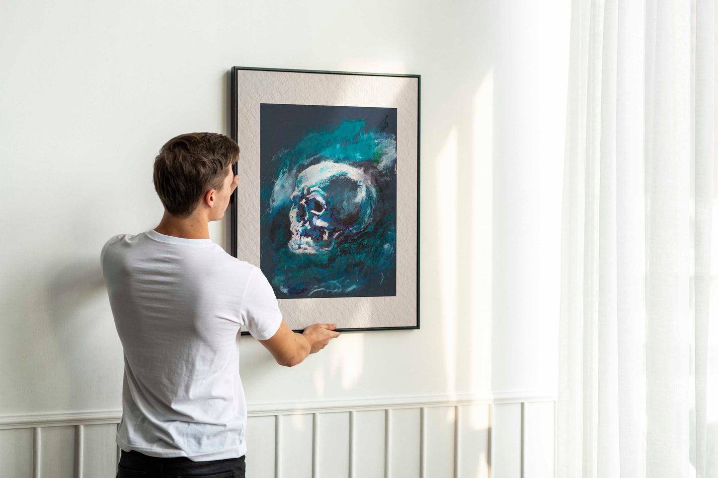 Person holding up framed Blue Remains fine art print by Bogdan Jensen on a wall, showing the blue skull study in a bright interior