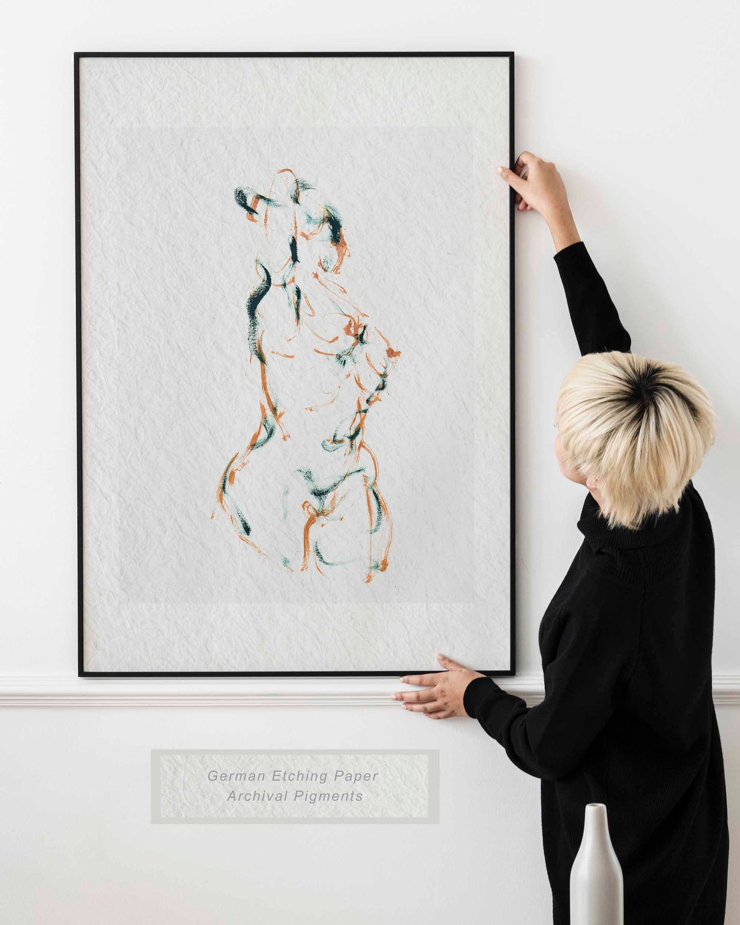 Lady holding framed Dancing into Form fine art print by Bogdan Jensen on a wall, showing the loose brown and blue-green figure drawing in a bright interior
