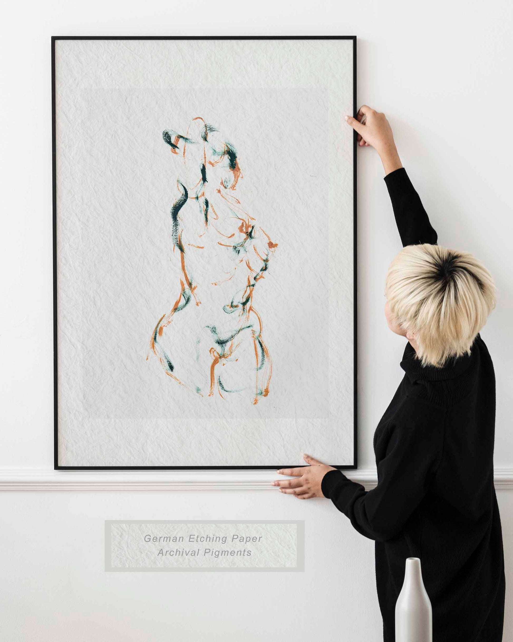 Lady holding framed Dancing into Form fine art print by Bogdan Jensen on a wall, showing the loose brown and blue-green figure drawing in a bright interior