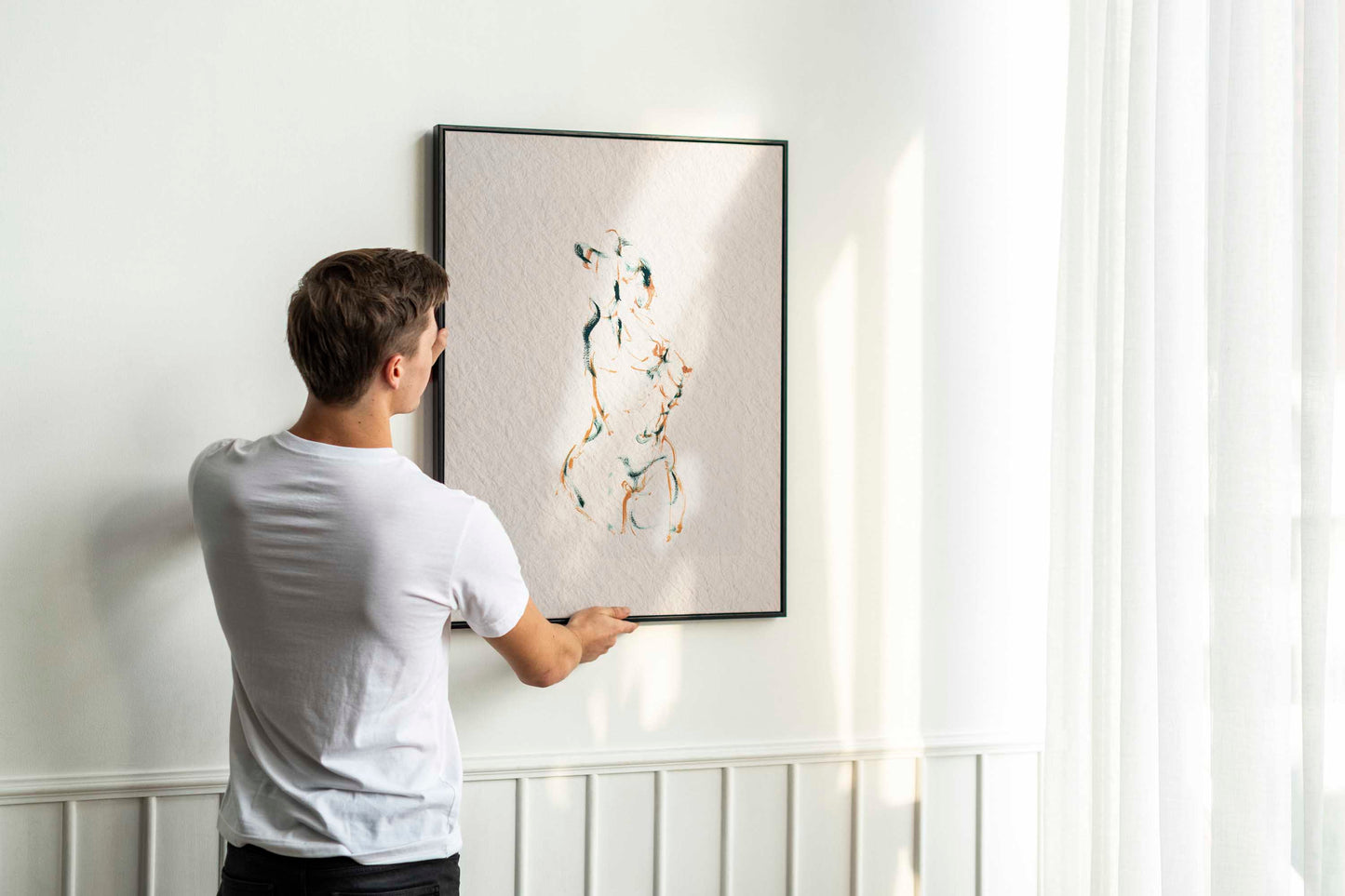 Person holding up framed Dancing into Form fine art print by Bogdan Jensen on a wall, showing the brown and blue-green figure drawing in a bright interior