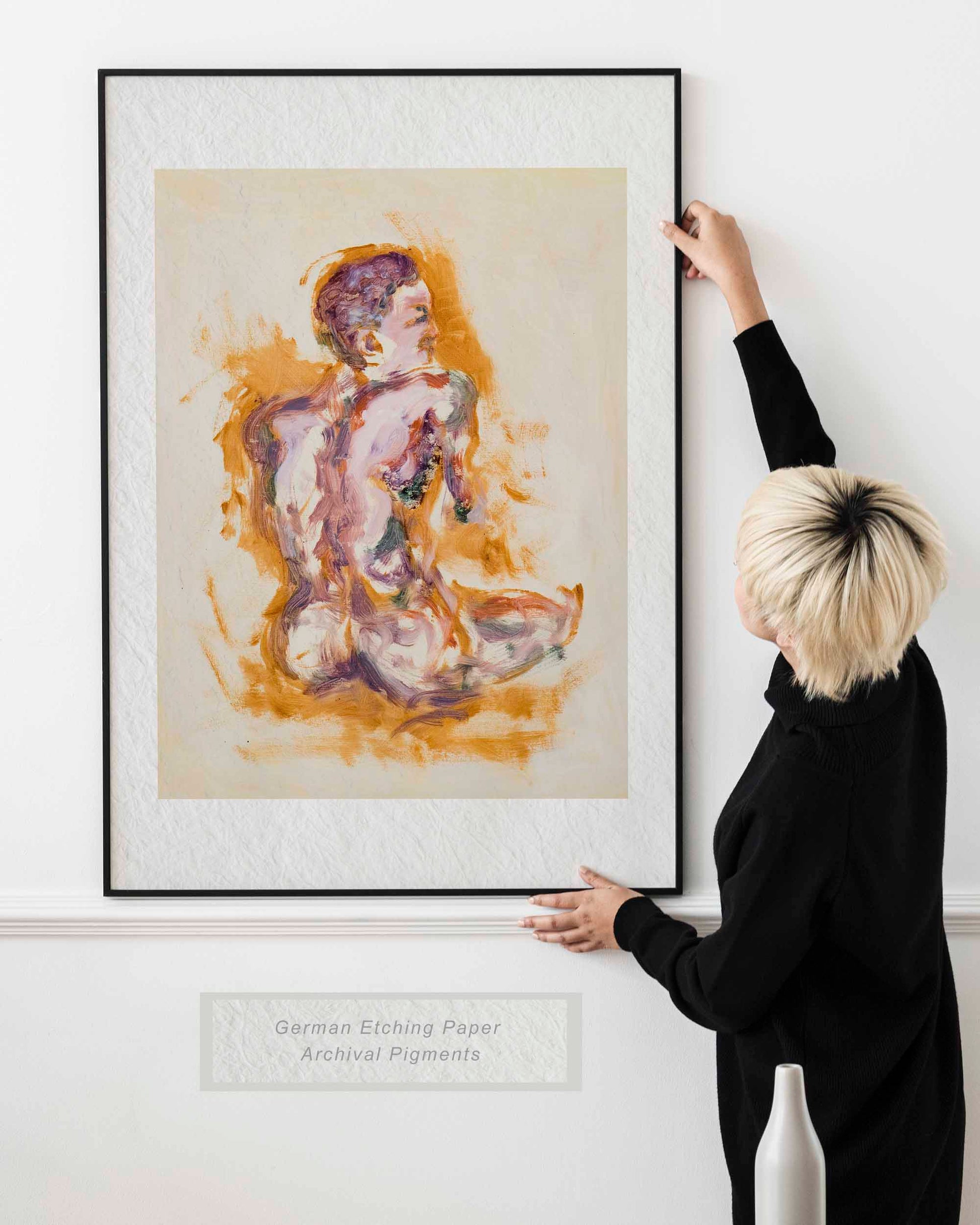 Woman holding framed Felt through Gold fine art print by Bogdan Jensen on a wall, showing the seated figure painting in lilac and gold tones in a bright interior