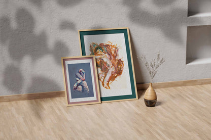Held by Fire fine art print by Bogdan Jensen shown leaning in a floor frame, with the reclining figure painting beside a smaller framed artwork