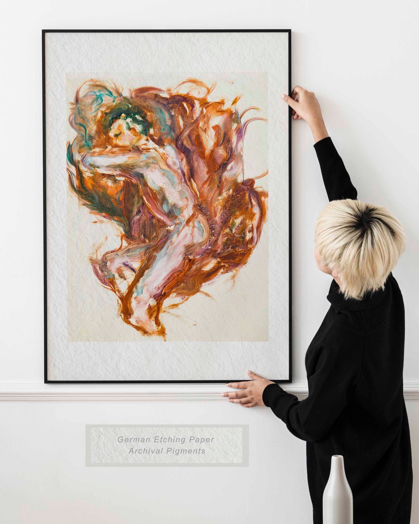 Woman holding framed Held by Fire fine art print by Bogdan Jensen on a wall, showing the reclining figure painting in copper, rose, and violet tones in a bright interior