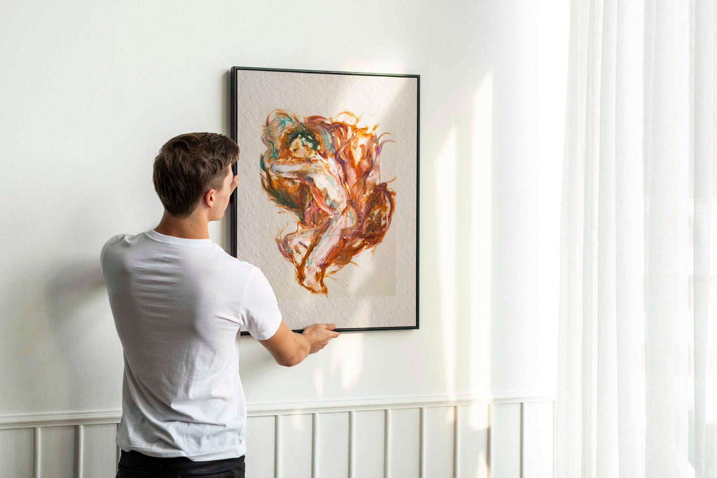 Person holding up framed Held by Fire fine art print by Bogdan Jensen on a wall, showing the reclining figure painting in warm copper and rose tones in a bright interior