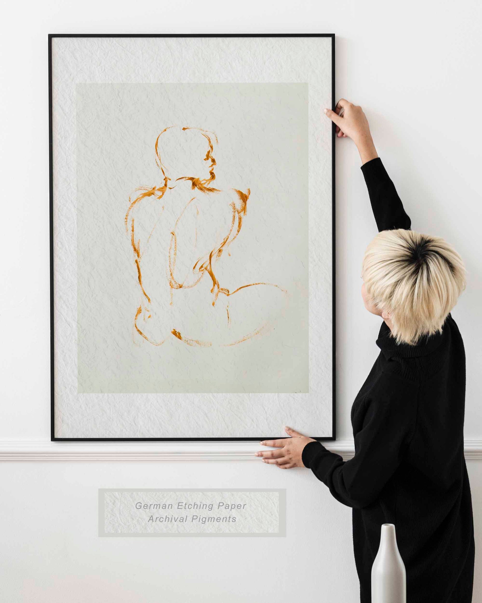 Woman holding framed Lost in Line fine art print by Bogdan Jensen on a wall, showing the minimal seated figure drawing in a bright interior