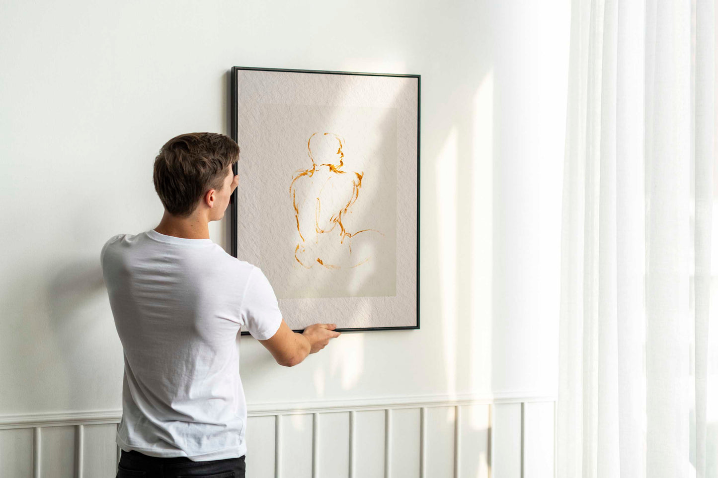 Person holding up framed Lost in Line fine art print by Bogdan Jensen on a wall, showing the warm ochre line drawing in a bright interior