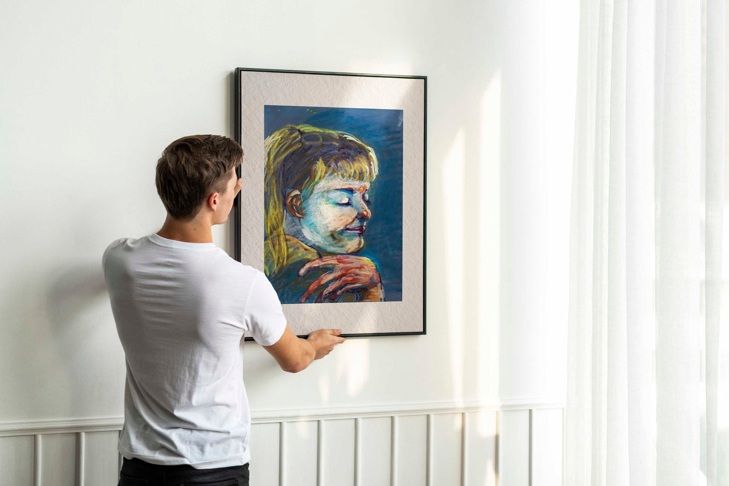 Person hanging framed Quiet Tide fine art print by Bogdan Jensen on a wall, showing the scale of the blue-toned pastel portrait