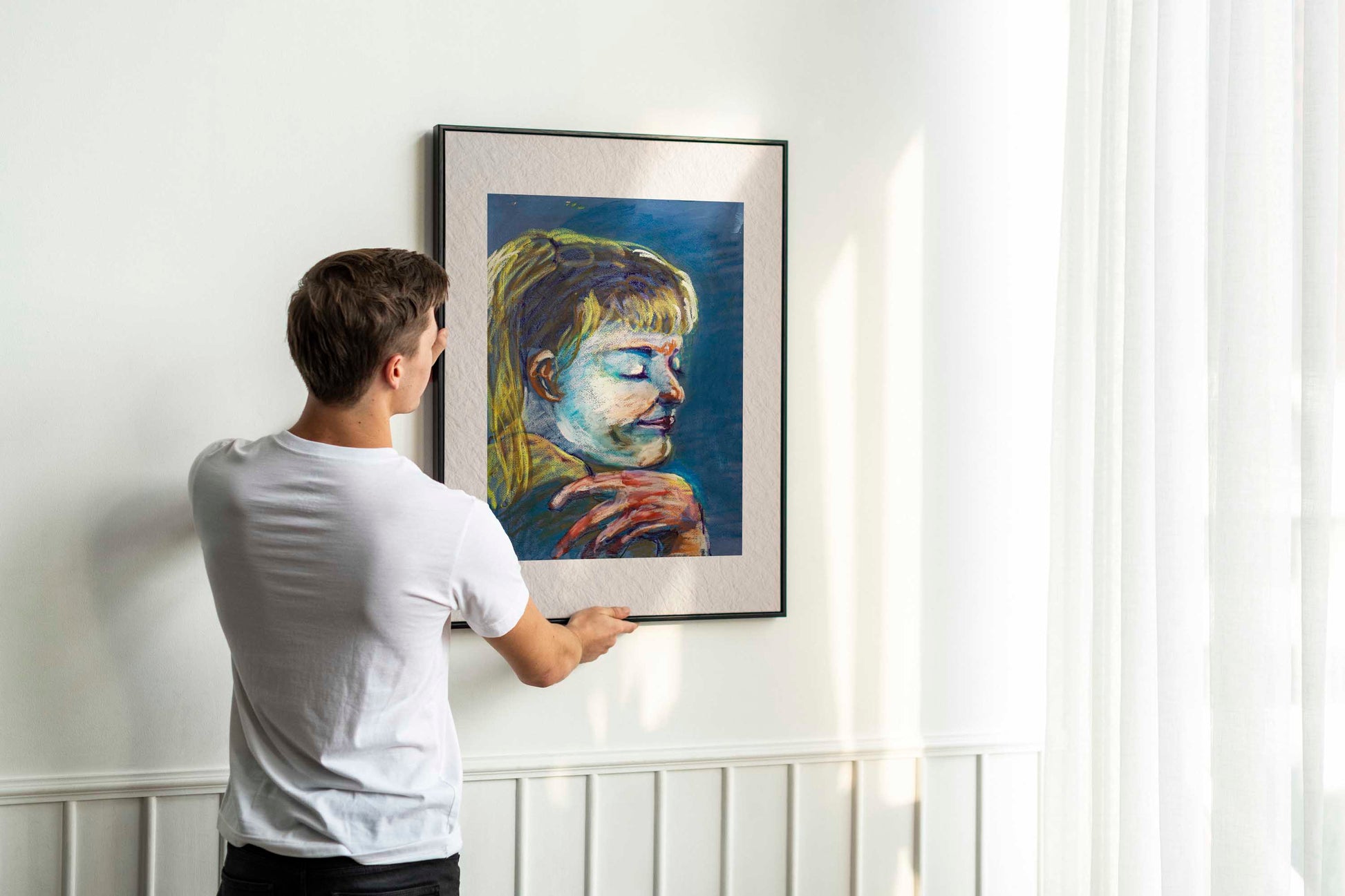 Person hanging framed Quiet Tide fine art print by Bogdan Jensen on a wall, showing the scale of the blue-toned pastel portrait