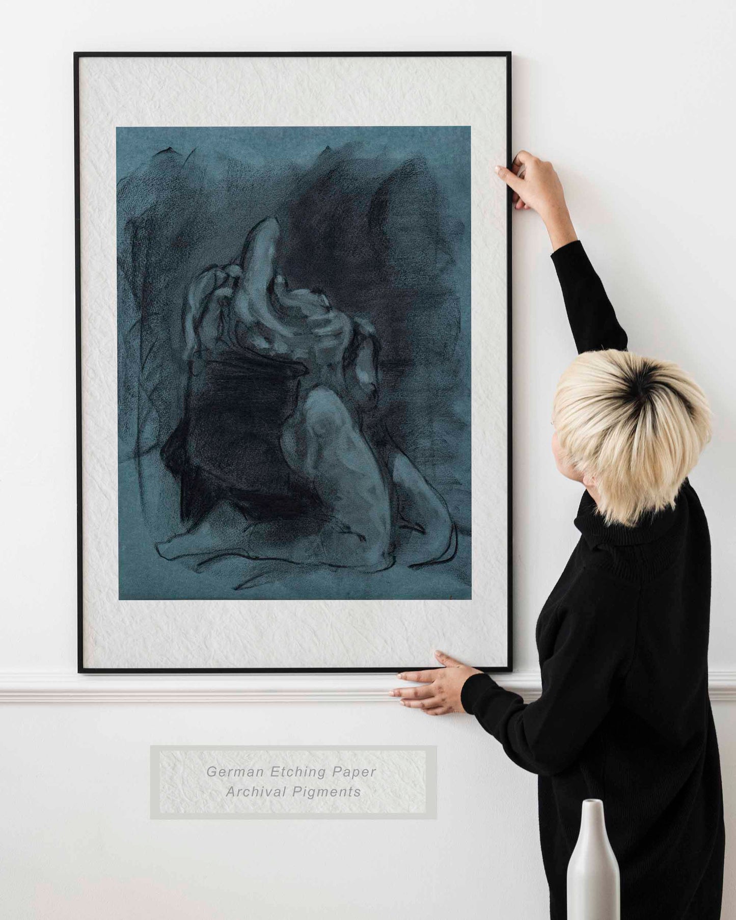 Woman holding framed Returned from Shadow fine art print by Bogdan Jensen on a wall, showing the dark blue charcoal figure drawing in a bright interior
