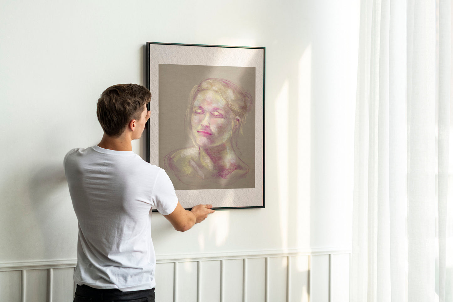 Person holding up framed Soft Glow fine art print by Bogdan Jensen on a wall, showing the pastel portrait in soft pink and yellow tones