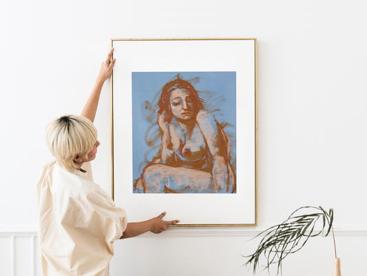Soft Whisper fine art print by Bogdan Jensen in a gold frame, shown being placed on a white wall as a large pastel figure study.