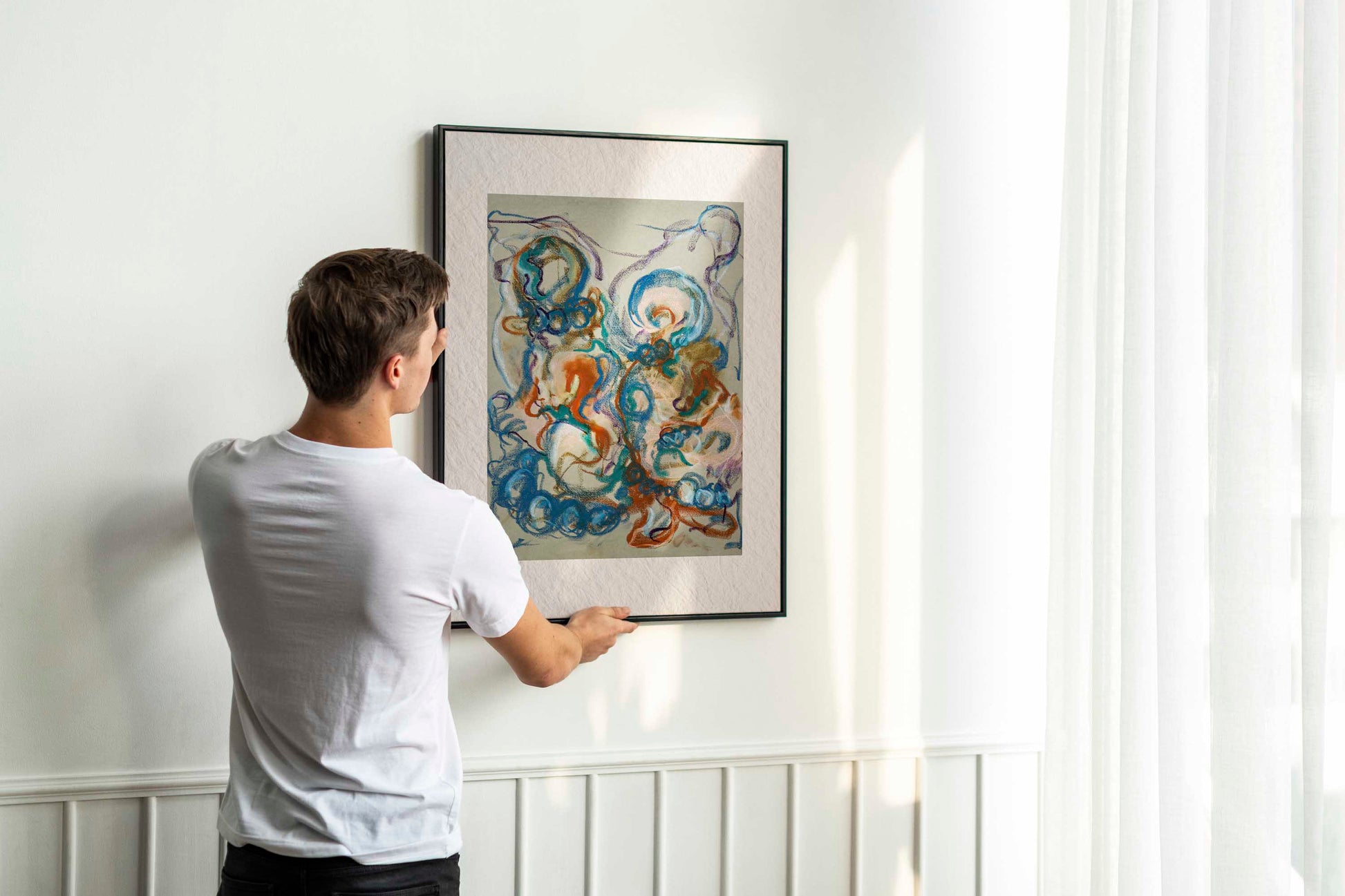 Person holding up framed Together in the Garlands fine art print by Bogdan Jensen on a wall, showing the colourful abstract figurative drawing in a bright interior