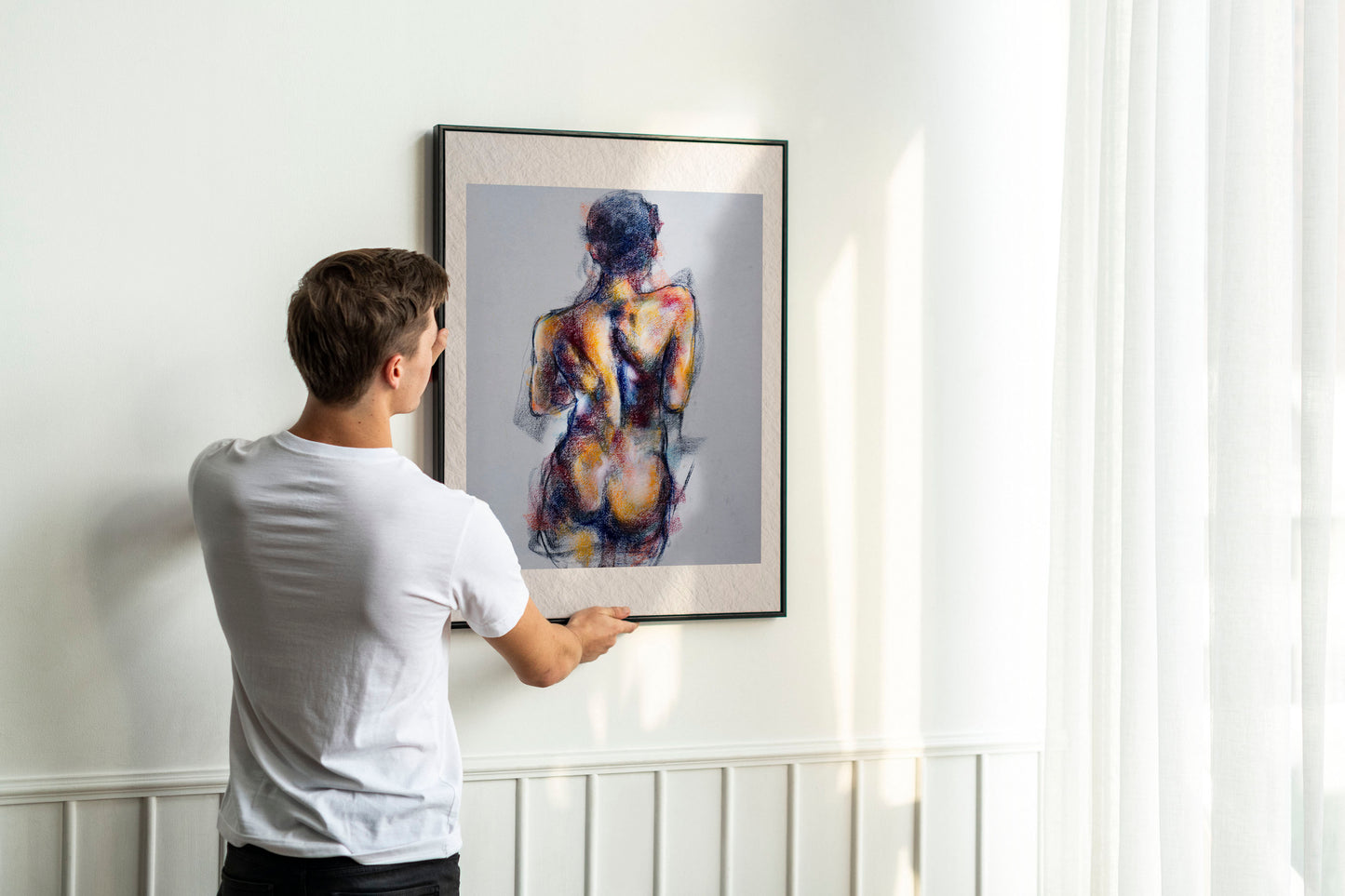 Person holding up framed Where the Dance Lives fine art print by Bogdan Jensen on a wall, showing the pastel figure study of a dancer’s back in a bright interior