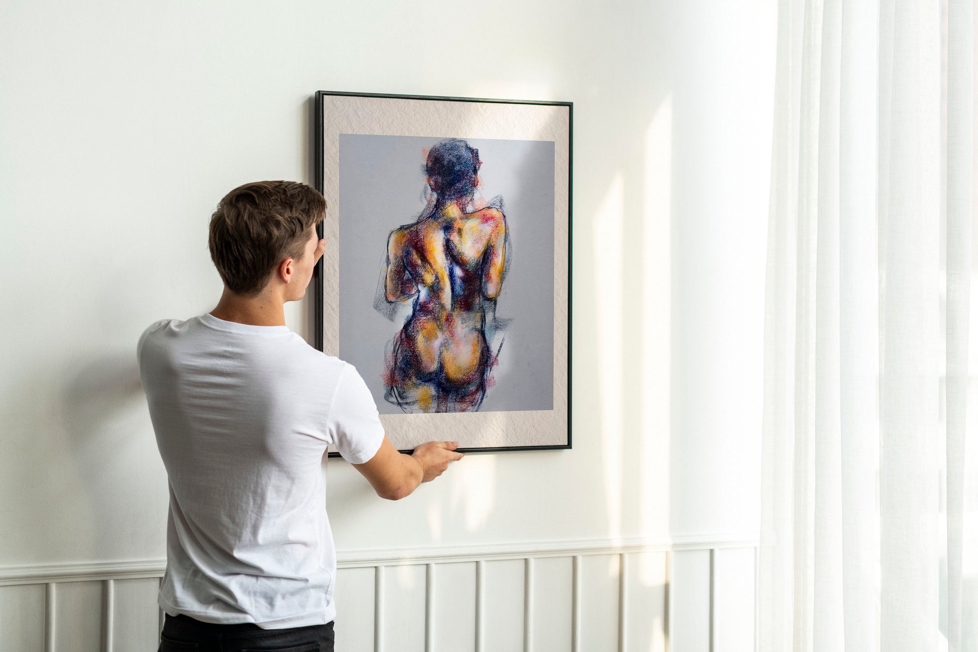 Person holding up framed Where the Dance Lives fine art print by Bogdan Jensen on a wall, showing the pastel figure study of a dancer’s back in a bright interior